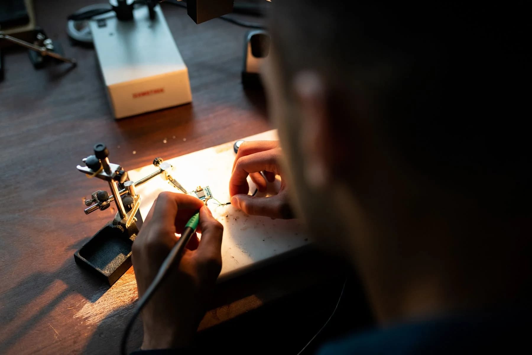 A person soldering a circuit board at a well-used workshop bench