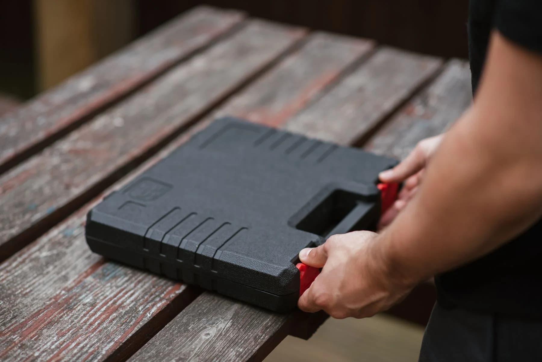 Hands opening a used tool case on a wooden workbench